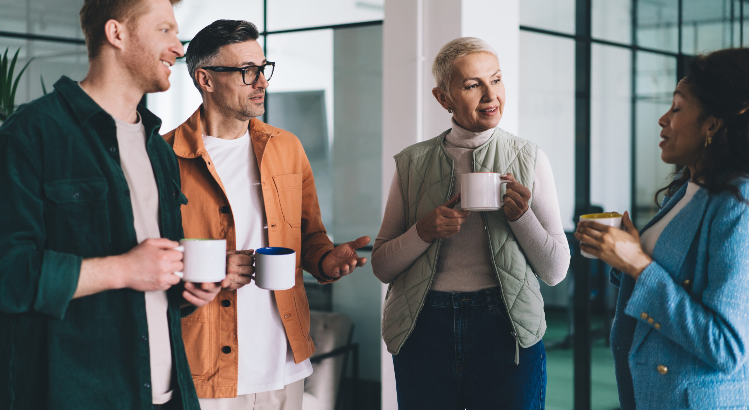 Confident male and female colleagues discussing exchange of experience in office, multicultural employees with coffee cups analyzing brainstorming teamwork and briefing