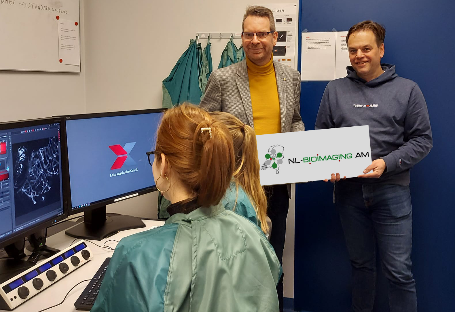 In the background, Ben Giepmans (left) and Eric Reits (right) proudly holding the NL-BioImaging sign. In the foreground, happy users at the microscopy facility. 